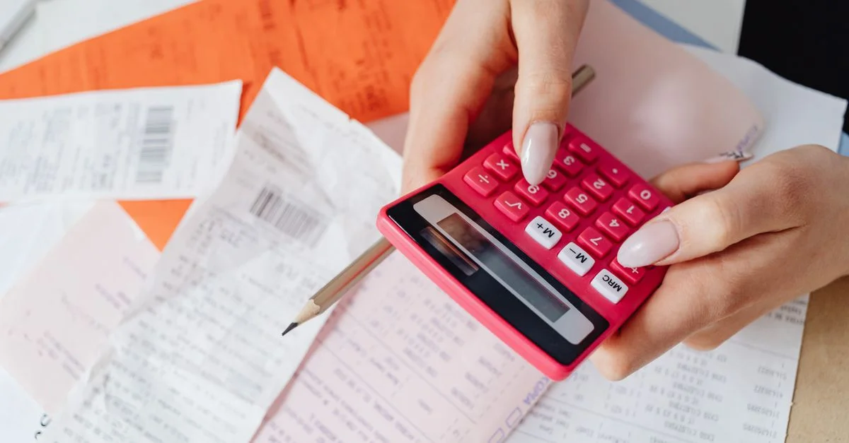 Mains utilisant une calculatrice rose pour gérer des dépenses parmi divers reçus et documents.
